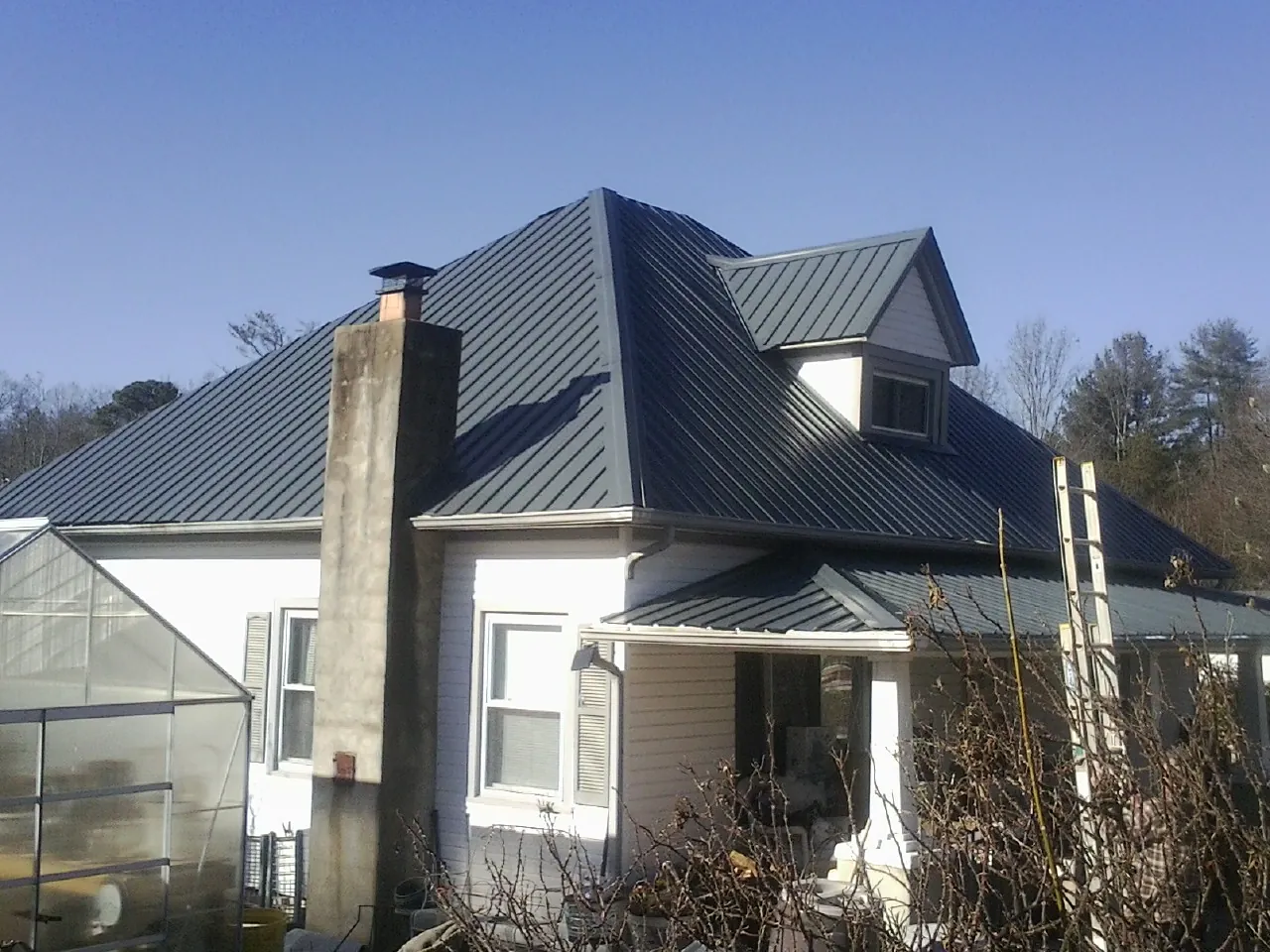 Dark blue standing seam metal roof on a white farmhouse with dormer — Slate & Tile Roof Repair by Roofing Brothers in Vernon Center