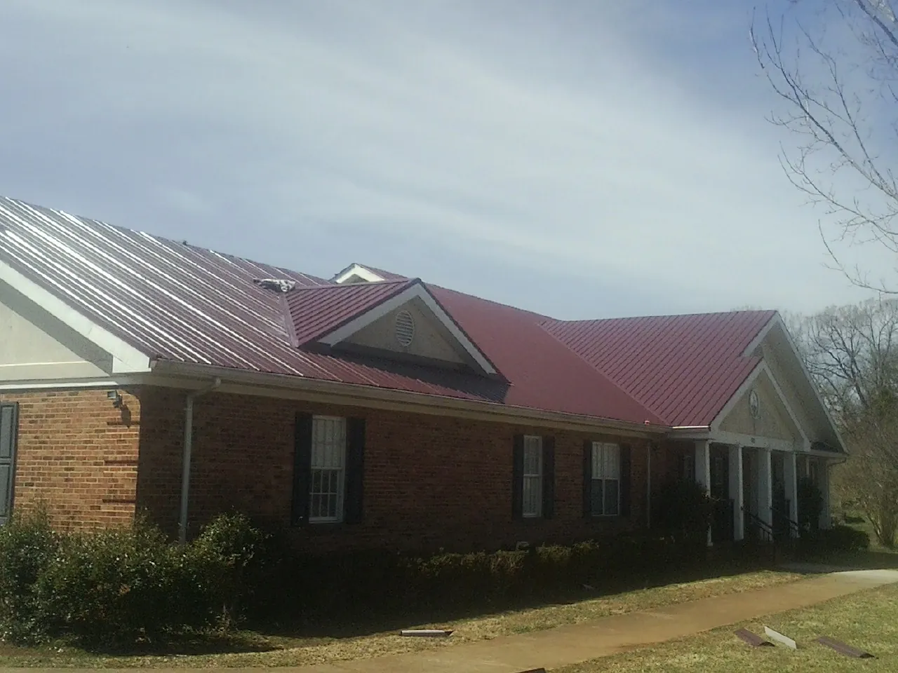 Red metal roof with gabled entries on a long brick building, from a Hail Damage Roof Repair job in Vernon Center