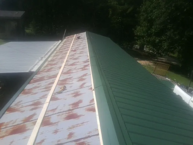 Old rusted panels beside newly installed green metal roofing — Wind Damage Roof Repair by Roofing Brothers in Vernon Center