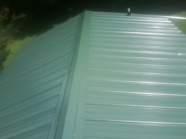 New green metal panels meeting at the ridge of a roof — Flat Roof Repair work by our crew in Vernon Center