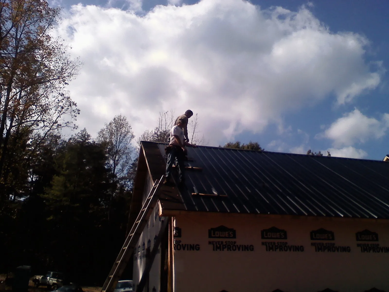 Roofer fastening dark metal panels high against a cloudy sky, from a Roof Inspection job in Vernon Center