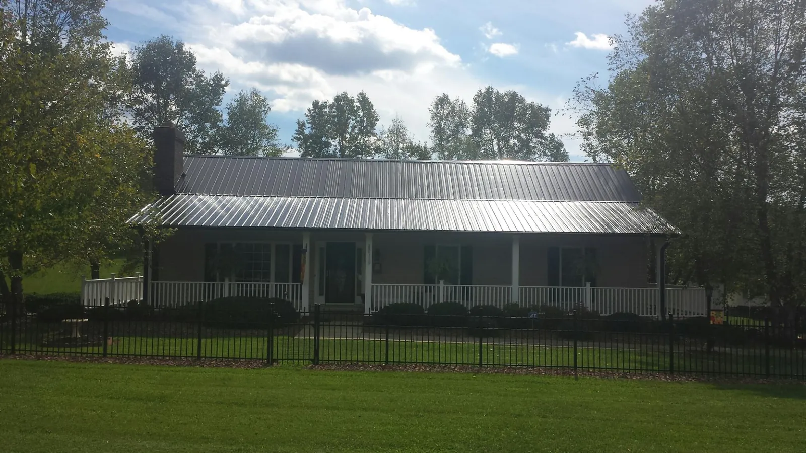 Gray metal roof on a brick ranch with a full width front porch — Gutter Guard Installation work by our crew in Vernon Center