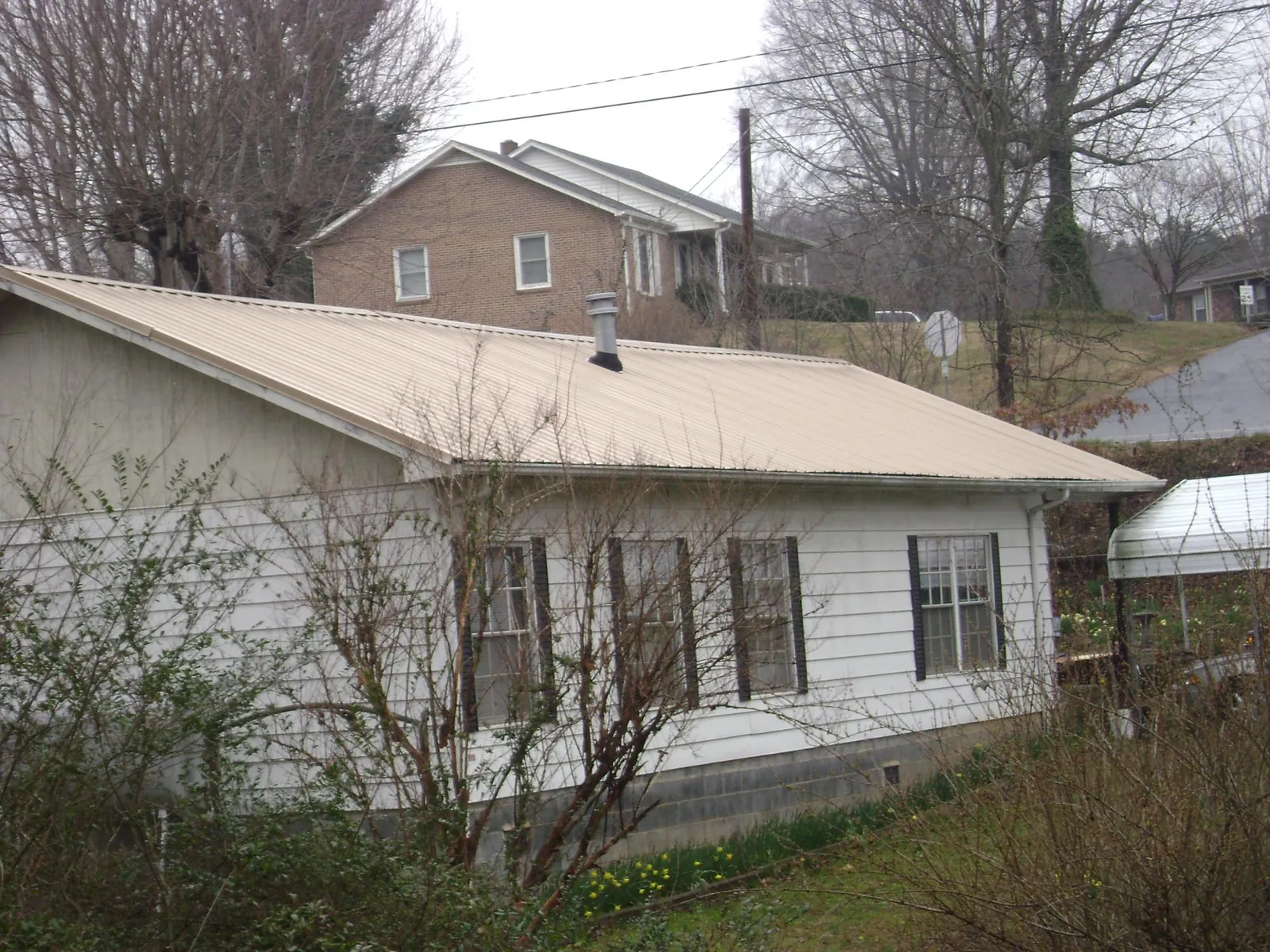 Tan metal roof on a white sided house set into a hillside — Commercial Roofing by Roofing Brothers in Vernon Center