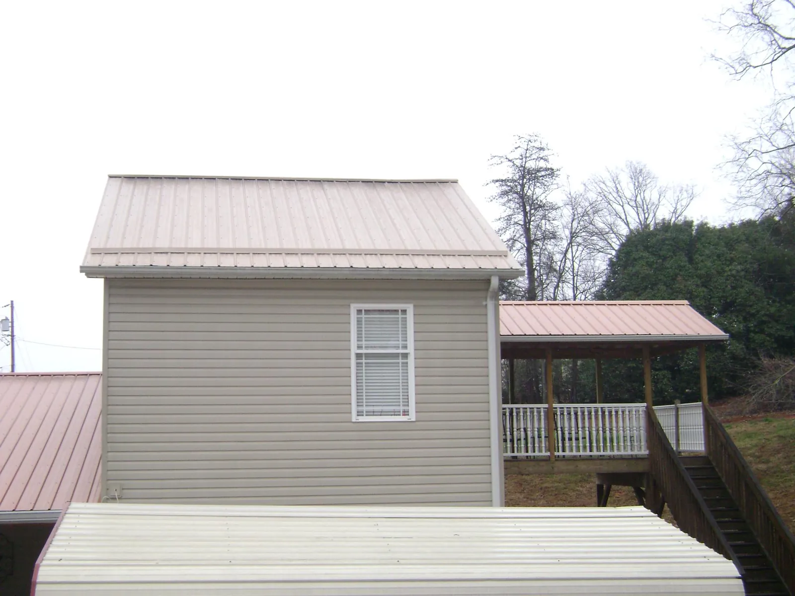 Tan metal roofs on a two story addition and attached porch, from a Roof Replacement job in Vernon Center